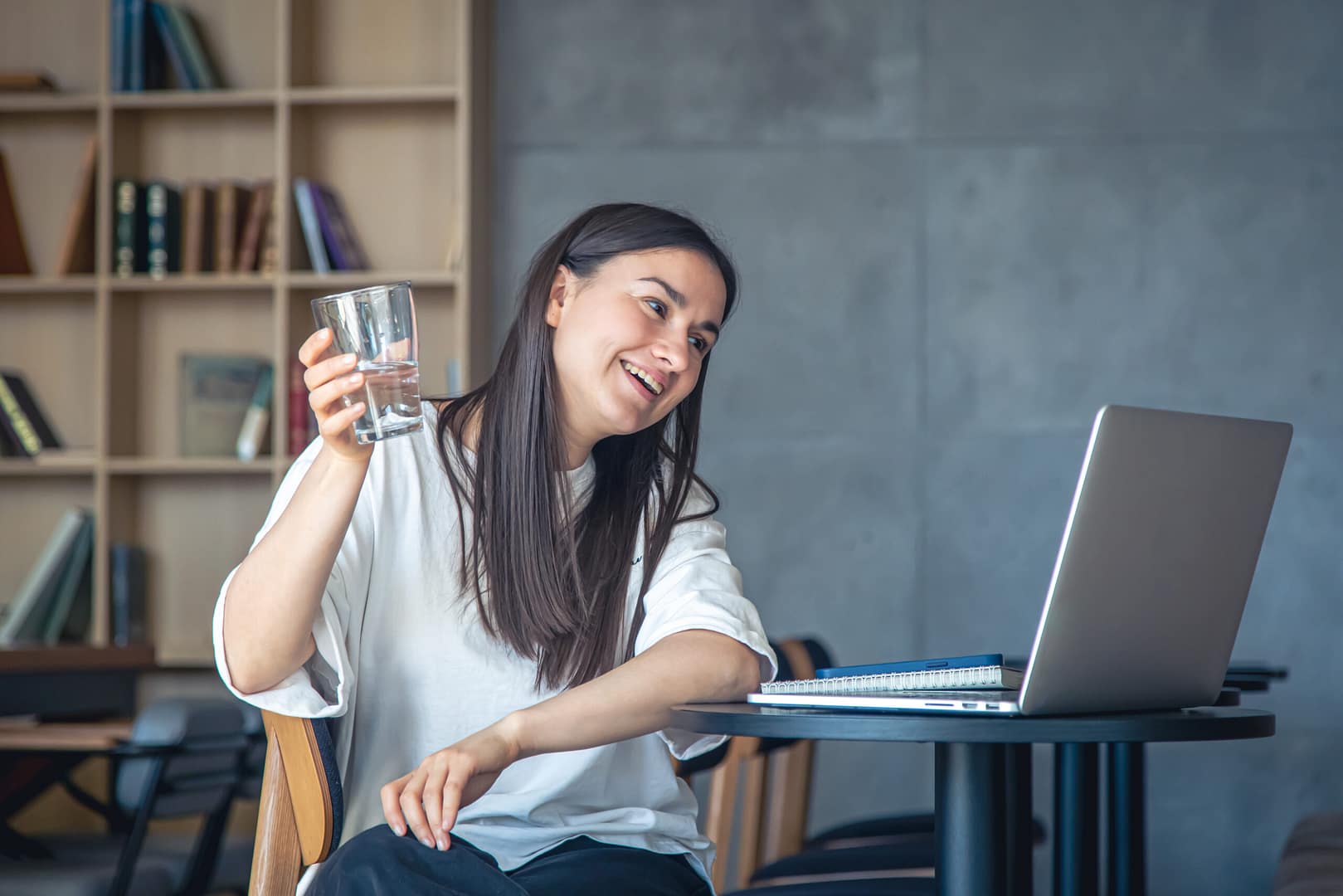 Young woman with a glass of water in front of a laptop.